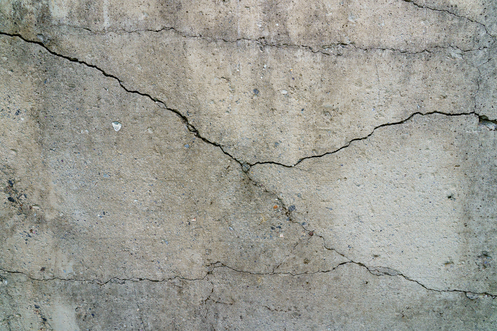 A close-up of a concrete wall with several visible cracks running across its surface.