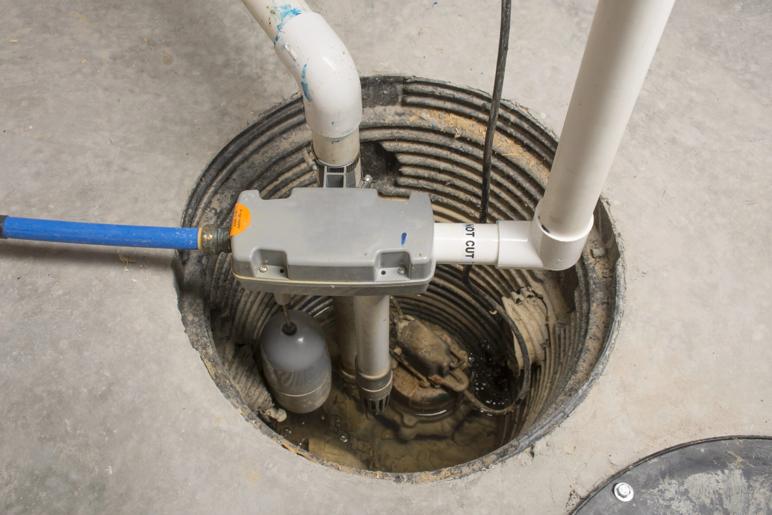 A sump pump system installed in a basement floor pit with connected PVC pipes and wiring visible.